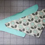 Zwei Stoffteile liegen auf einer Schneidematte. Ein Teil ist mintgrün, das andere hat ein Blumenmuster. Ein Schnittmuster für ein Halstuch Baby.