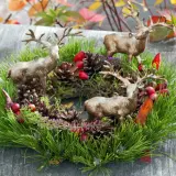 Drei Hirschfiguren schmücken einen grünen Kranz mit Tannenzweigen, Zapfen und roten Beeren. Tolle Herbstkranz Ideen für Ihr Zuhause.