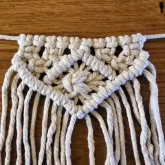 Detailaufnahme einer Makramee-Wimpelkette mit Anleitung. Die Kette ist aus weißer Schnur geknüpft und zeigt ein komplexes Muster.