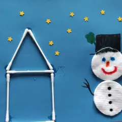 Ein fröhlicher schneemann aus wattepads steht vor einem Haus aus Wattestäbchen. Kleine gelbe Sterne funkeln am blauen Himmel.