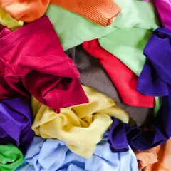 Bunte Stoffe, bereit für T-Shirt Upcycling. Ein Berg aus Rot, Lila, Grün, Gelb und Orange lädt zum kreativen Gestalten ein.
