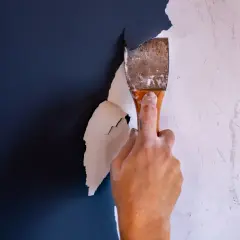 Hand schabt mit einem Spachtel die alte Farbe ab. Der Prozess, Farbe entfernen, beginnt.