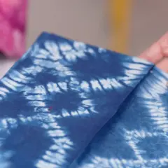 Hände falten ein tiefblaues Tuch mit dem Muster der Shibori Technik.