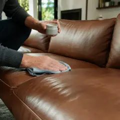 Mann pflegt braunes Ledersofa mit einem Tuch und einer Creme. Einfache lederpflege hausmittel für ein schönes Zuhause.