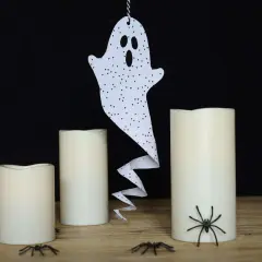Ein ausgeschnittenes Gespenst mit Punkten hängt über drei Kerzen. Spinnen krabbeln auf dem Tisch.