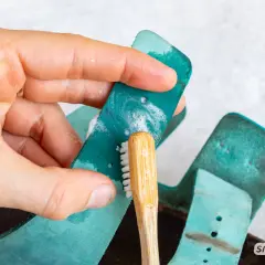 Hand reinigt türkisfarbene Birkenstock-Riemen mit einer kleinen Bürste und Seife. So einfach ist das Birkenstock reinigen!