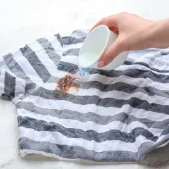 Flüssigkeit wird auf einen Fleck auf einem gestreiften T-Shirt gegossen, um Wandfarbe aus Kleidung zu entfernen.