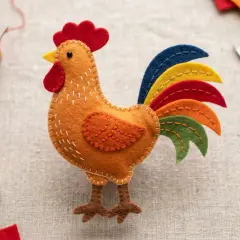 Ein farbenfrohes Huhn aus Filz, bereit zum Huhn filzen. Nadel, Faden und Schere liegen daneben.