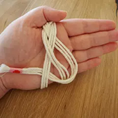 Hand hält cremefarbene Schnur für makramee serviettenringe anleitung. Ein Teil ist mit rosa Band umwickelt.