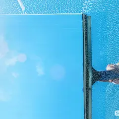 Fensterputzen mit Glycerin: Ein klarer Blick auf den blauen Himmel, während eine Hand mit einem Abzieher über das seifige Glas gleitet.