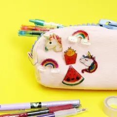Bunte Schrumpffolie Ideen: Einhorn, Regenbogen, Pommes & Wassermelone zieren eine Federtasche. Stifte & Klebeband liegen daneben.