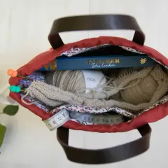 Kreative Ideen für upcycling taschen selber machen: Wolle, Stricknadeln, ein Buch und Maßband in einer roten Tasche.