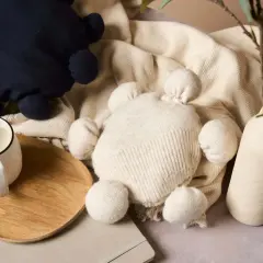 Zwei Kuscheltiere, eines dunkelblau, das andere cremefarben, liegen auf einer Decke. Ein Becher Kaffee steht auf einem Holztablett. Kreatives **Pullover Upcycling** für süße Spielzeuge.
