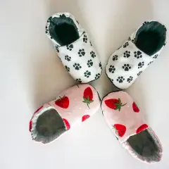 Zwei Paar süße Babyschuhe: eins mit Pfotenabdrücken, eins mit Erdbeeren. Hier findest du ein schnittmuster babyschuhe kostenlos zum Nachnähen!