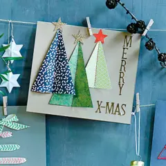 Moderne weihnachtskarten basteln: Karten mit Bäumen, Sternen und Schriftzug "Merry X-Mas" hängen an einer Schnur.