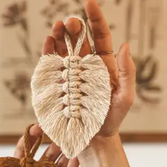 Eine Hand hält eine Makramee Feder. Die Anleitung für diese Feder ist einfach und das Ergebnis ist ein schönes Deko-Objekt.