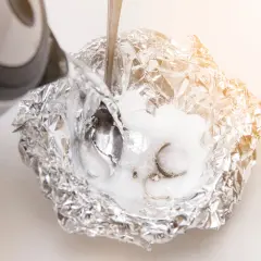 Silber putzen mit Natron: Heißes Wasser wird über Aluminiumfolie mit Natron und Schmuck gegossen, um angelaufenes Silber zu reinigen.