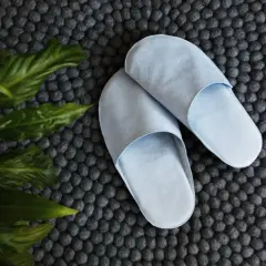 Zwei hellblaue Hausschuhe liegen auf einem dunklen Filzteppich neben grünen Blättern. Perfekt für alle, die Hausschuhe selber machen wollen.