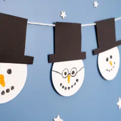 Schneemann-Girlande als winter bastelideen kinder. Weiße Kreise mit schwarzen Hüten und Gesichtern hängen an einer Schnur.