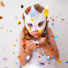 Ein Mädchen mit Einhorn-Faschingsmaske bläst Konfetti. Eine tolle Vorlage für deine nächste Party!