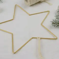 Goldener Sternrahmen für Makramee Weihnachten, umgeben von Tannenzweigen und weißen Kugeln.