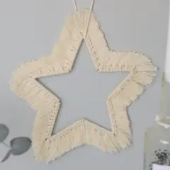Ein Makramee Stern an der Wand, der wie eine Anleitung zum Nachbasteln aussieht.