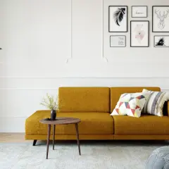 Ein gemütliches kleines Wohnzimmer einrichten mit einem senfgelben Sofa, Kissen, einem Beistelltisch und Wandkunst.
