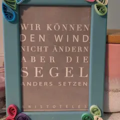 Ein hellblauer Bilderrahmen mit Quilling-Verzierungen, der ein Zitat von Aristoteles zeigt: "Wir können den Wind nicht ändern, aber die Segel anders setzen". Eine schöne alte Bilderrahmen Deko Idee.