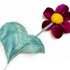 Stoffblumen selber machen: Eine lila Blüte mit gelbem Zentrum und ein grünes Blatt aus Stoff, auf weißem Grund.