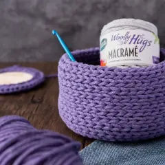 Ein lila gehäkelter Korb mit Garnrolle und Häkelnadel. Perfekt für eine makramee korb anleitung.