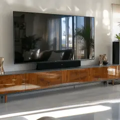 Modernes Wohnzimmer mit großem Fernseher über einem stilvollen deko tv board aus Holz. Lautsprecher und Pflanzen ergänzen das Ambiente.