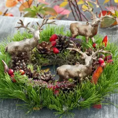 Drei Hirschfiguren schmücken einen grünen Kranz mit Tannenzweigen, Zapfen und roten Beeren. Tolle Herbstkranz Ideen für Ihr Zuhause.