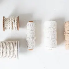 Verschiedene Garne für Makramee: dicke und dünne Schnüre in Weiß und Beige, aufgewickelt auf Spulen und Rollen.