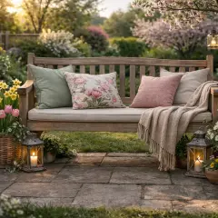 Eine einladende Gartenbank, liebevoll dekoriert mit Kissen, Decke und Blumen. Perfekt, um den Frühling zu genießen.