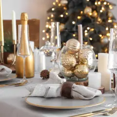 Moderne tischdeko weihnachten: Goldene Kugeln, Kerzen und Champagnergläser auf festlich gedecktem Tisch vor beleuchtetem Weihnachtsbaum.