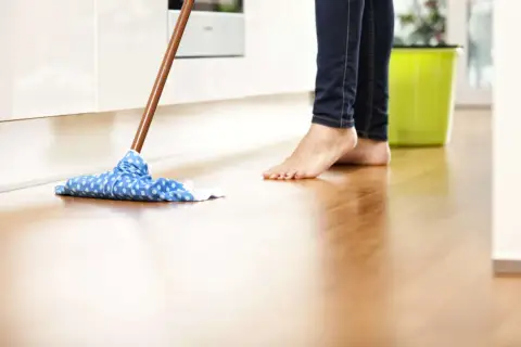 Barfuß wird der Holzboden mit einem blauen Wischmopp gereinigt. Was ist Schmierseife? Sie ist ein natürliches Reinigungsmittel, das sich gut für Böden eignet.