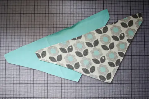 Zwei Stoffteile liegen auf einer Schneidematte. Ein Teil ist mintgrün, das andere hat ein Blumenmuster. Ein Schnittmuster für ein Halstuch Baby.