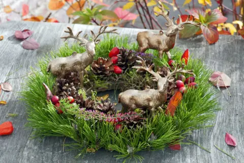 Drei Hirschfiguren schmücken einen grünen Kranz mit Tannenzweigen, Zapfen und roten Beeren. Tolle Herbstkranz Ideen für Ihr Zuhause.