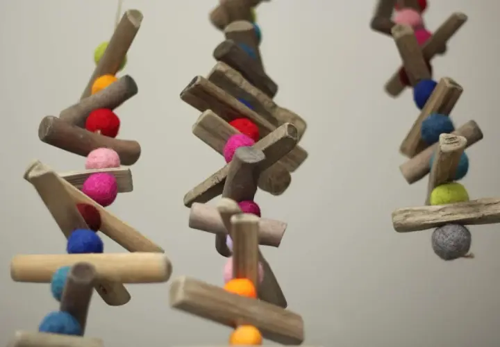 Bunte Filzkugeln und Holzstücke hängen an Schnüren. Tolle nadelfilzen ideen für Deko oder Vogelfutter.