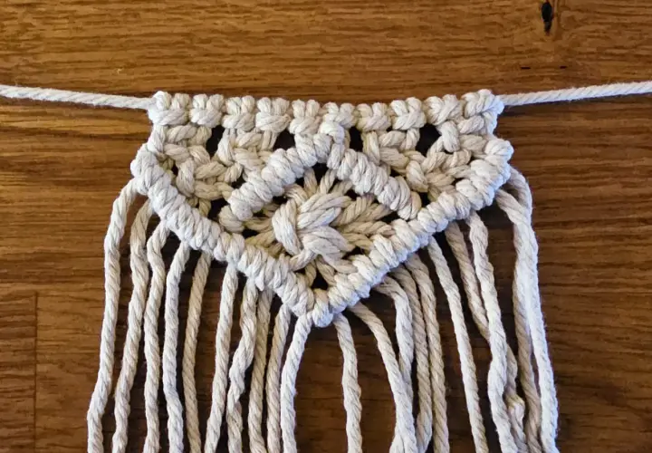 Detailaufnahme einer Makramee-Wimpelkette mit Anleitung. Die Kette ist aus weißer Schnur geknüpft und zeigt ein komplexes Muster.