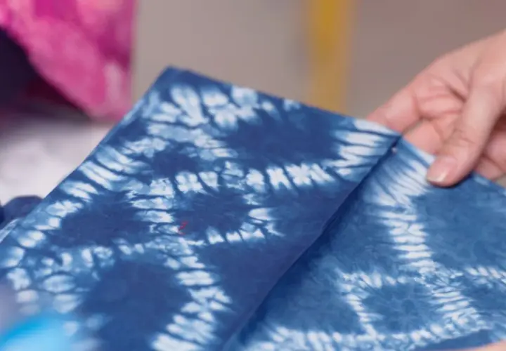 Hände falten ein tiefblaues Tuch mit dem Muster der Shibori Technik.
