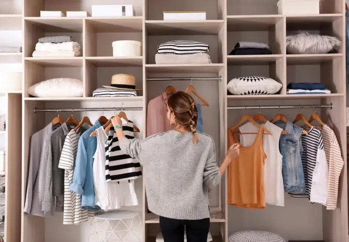 Frau sortiert Kleidung im offenen Kleiderschrank. Hier sind clevere Kleiderschrank Aufteilung Tipps für Ordnung.