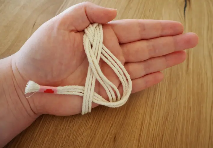 Hand hält cremefarbene Schnur für makramee serviettenringe anleitung. Ein Teil ist mit rosa Band umwickelt.