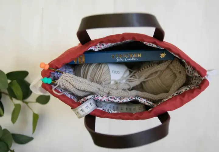 Kreative Ideen für upcycling taschen selber machen: Wolle, Stricknadeln, ein Buch und Maßband in einer roten Tasche.