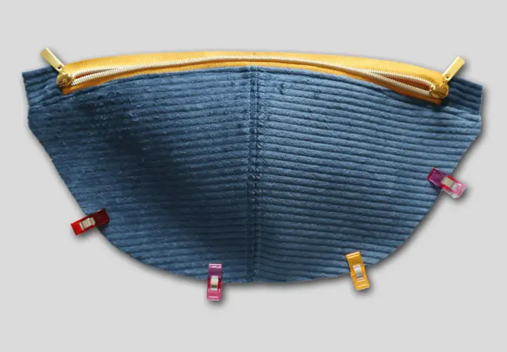 Blauer Cordstoff mit Reißverschluss und Nähklammern, bereit für das Schnittmuster einer Bauchtasche.
