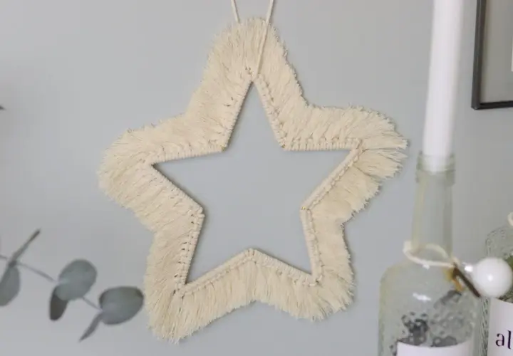 Ein Makramee Stern an der Wand, der wie eine Anleitung zum Nachbasteln aussieht.