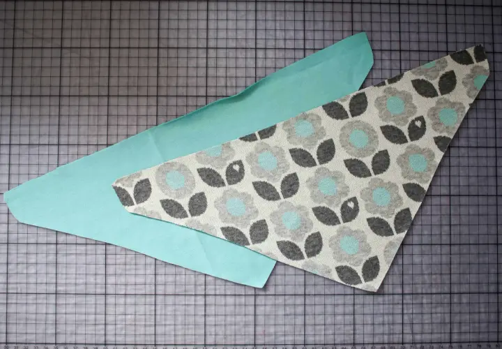 Zwei Stoffteile liegen auf einer Schneidematte. Ein Teil ist mintgrün, das andere hat ein Blumenmuster. Ein Schnittmuster für ein Halstuch Baby.