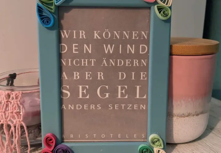 Ein hellblauer Bilderrahmen mit Quilling-Verzierungen, der ein Zitat von Aristoteles zeigt: "Wir können den Wind nicht ändern, aber die Segel anders setzen". Eine schöne alte Bilderrahmen Deko Idee.
