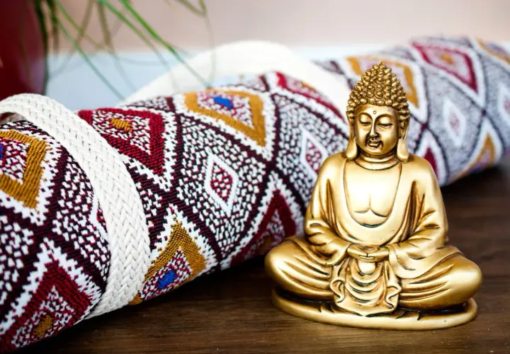 Goldene Buddha-Figur neben einer gerollten Yogamatte mit ethnischem Muster. Vielleicht das Schnittmuster für eine Yogatasche?
