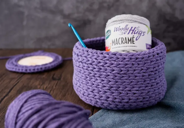 Ein lila gehäkelter Korb mit Garnrolle und Häkelnadel. Perfekt für eine makramee korb anleitung.